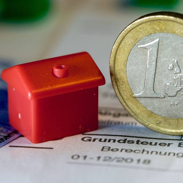 Eine Euro-Geldmünze sowie ein Spielzeughaus stehen auf einem Abgabenbescheid für die Entrichtung der Grundsteuer.