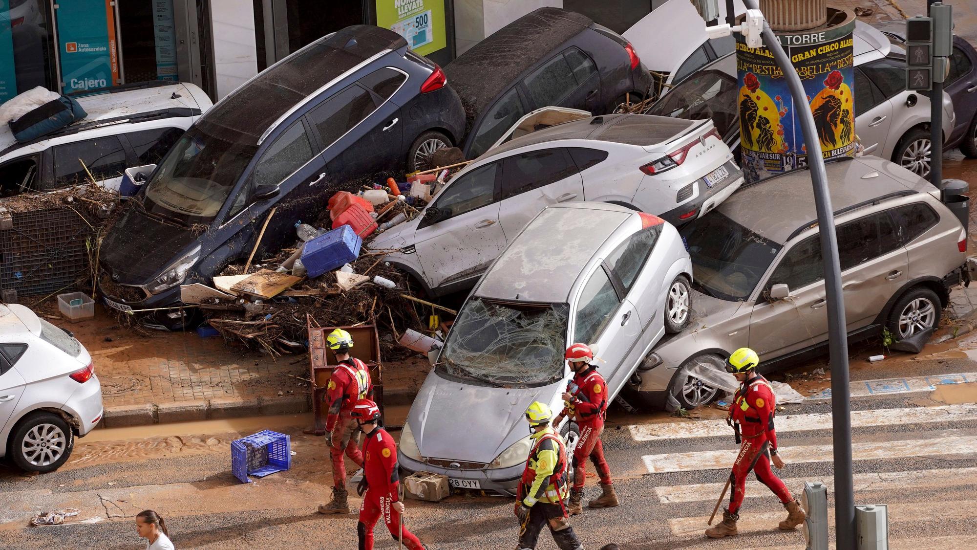 Rettungskräfte gehen an aufgestapelten Autos vorbei, die von den Überschwemmungen weggeschwemmt wurden.