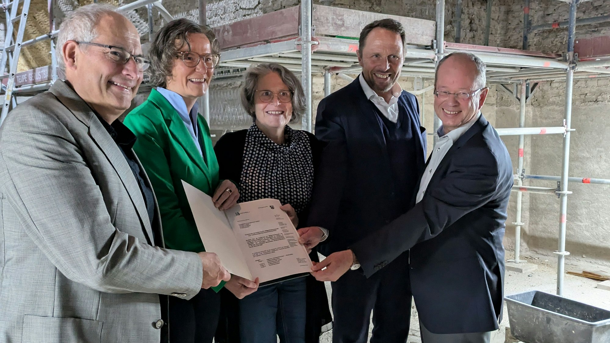 Vier Männer und eine Frau halten ein Dokument in einer Baustelle