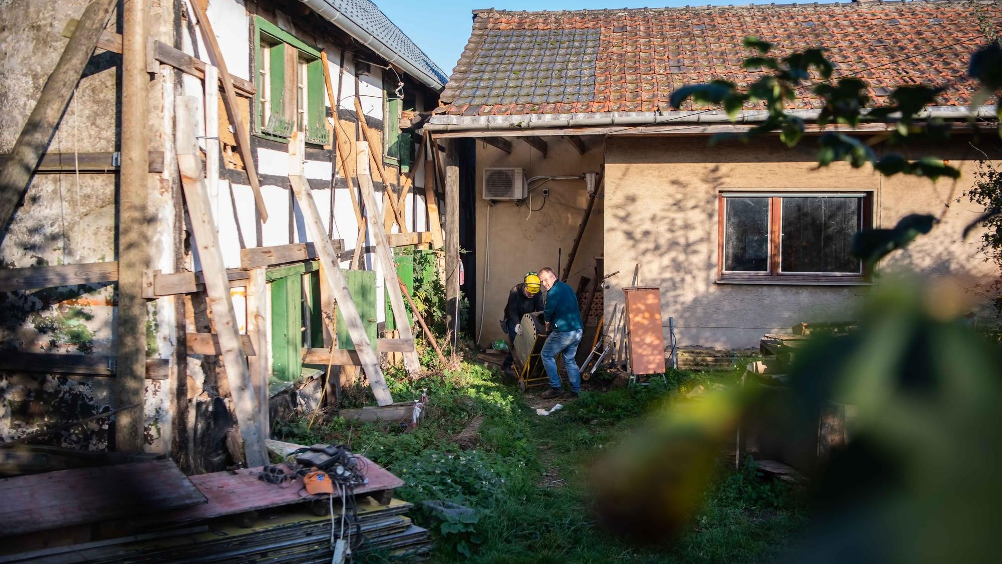 Das Bild zeigt zwei Helfer, die gerade einen Ofen aus dem Fachwerkhaus bei Lommersum wuchten.