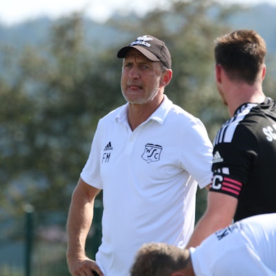 Co-Trainer Frank Marwitz trägt ein weißes Poloshirt. Neben ihm steht ein Fußballspieler im schwarzen Trikot.
