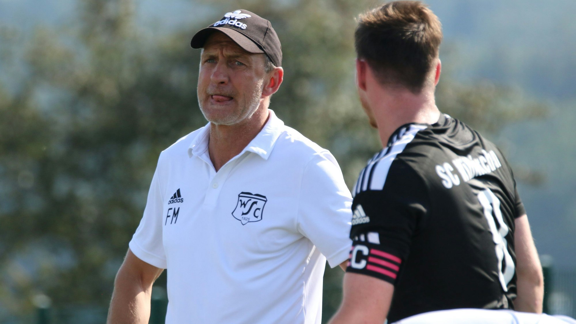 Co-Trainer Frank Marwitz trägt ein weißes Poloshirt. Neben ihm steht ein Fußballspieler im schwarzen Trikot.