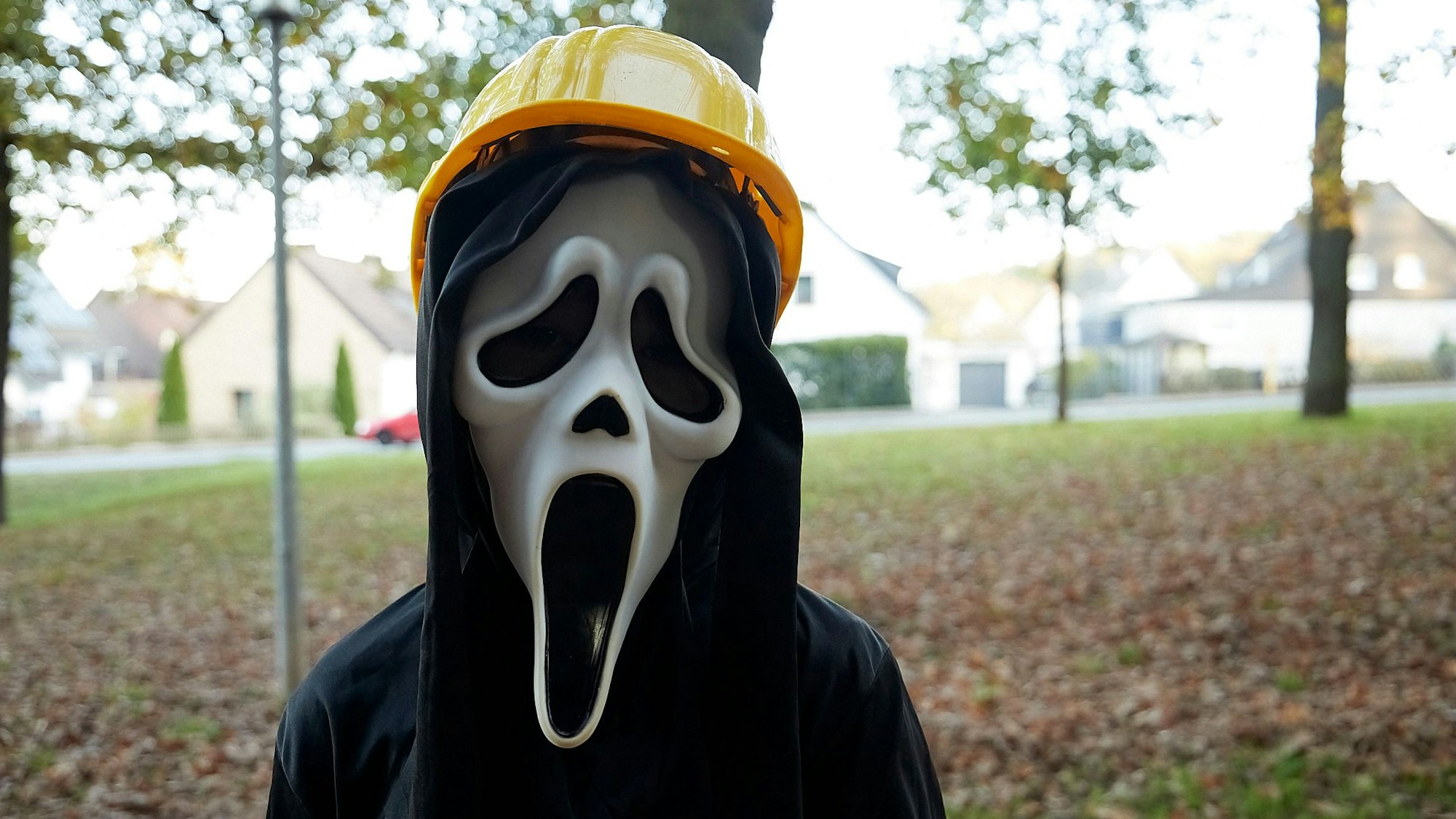 Ein Mädchen ist zu Halloween als Gruselbergmann mit Scream-Maske und gelbem Bauarbeiter-Helm verkleidet.