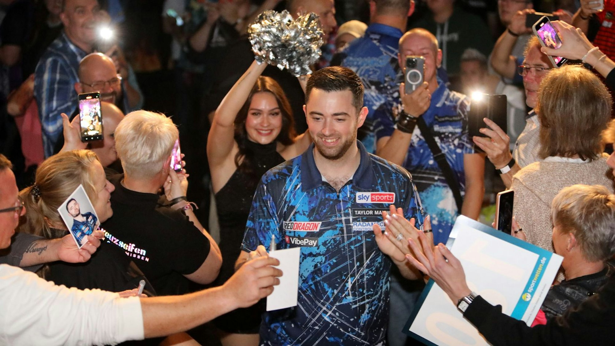 Ein Mann ist umringt von Menschen, die klatschen und Autogrammzettel hinhalten.