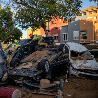 Zwei Feuerwehrleute arbeiten in einem von dem Unwetter betroffenen Gebiet und klettern über zerstörte Autos.
