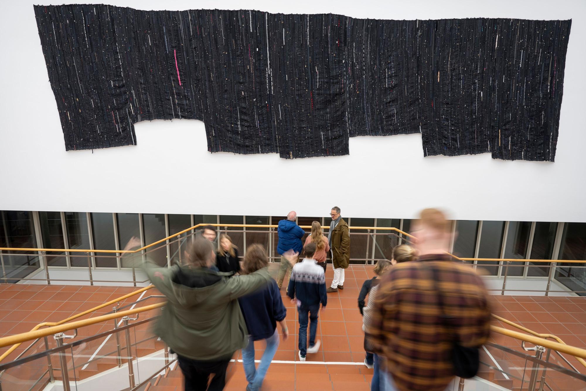 Museumsnachtbesucher vor Kresiah Mukwazhis Werk im Museum Ludwig: Ein Wandteppich aus BH-Trägern bildet eine große schwarze Fläche.