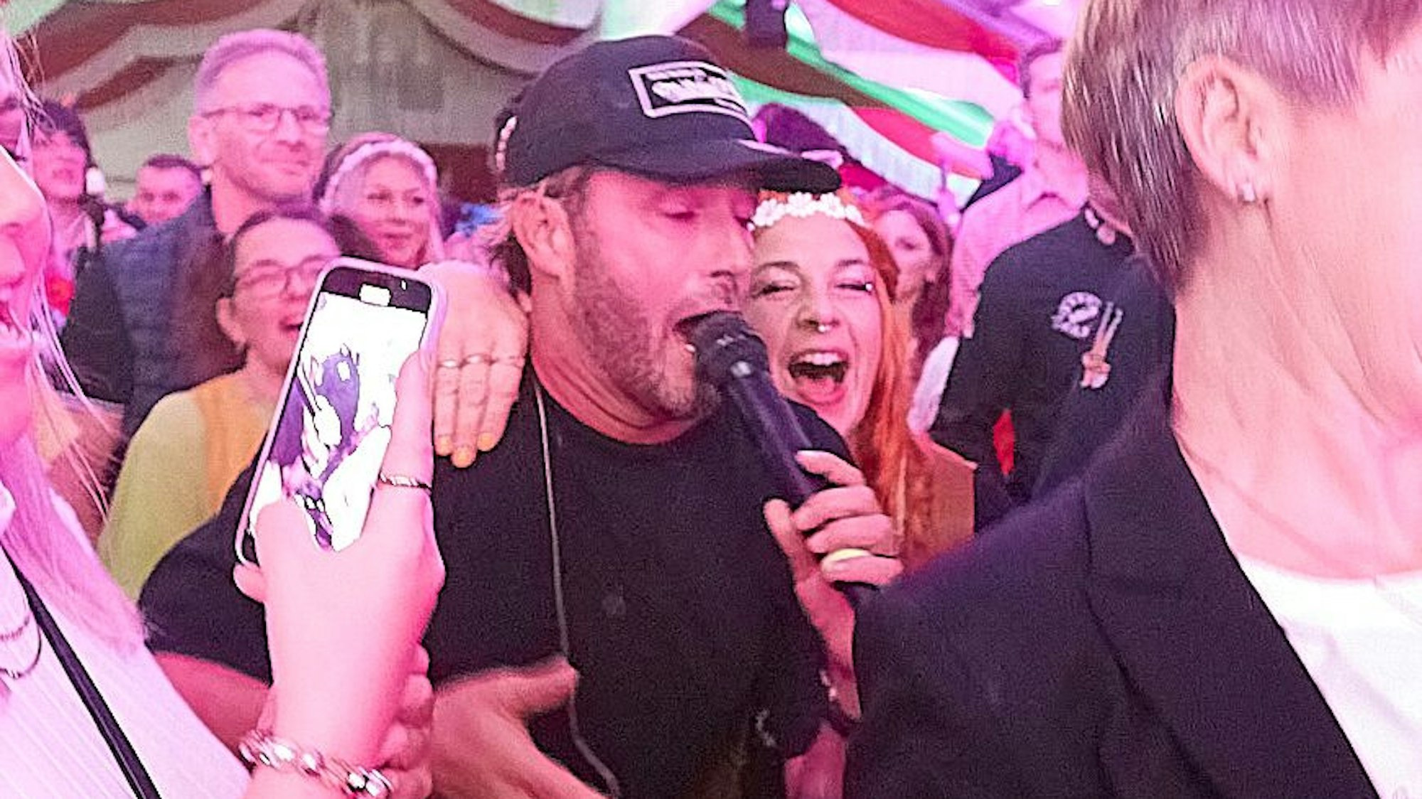 Ein Mann mit Kappe singt in einer Menge in ein Mikrofon.