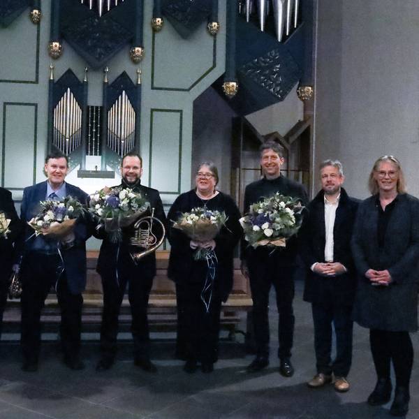 Acht Menschen schauen in Richtung der Kamera, sechs von ihnen halten Blumensträuße.