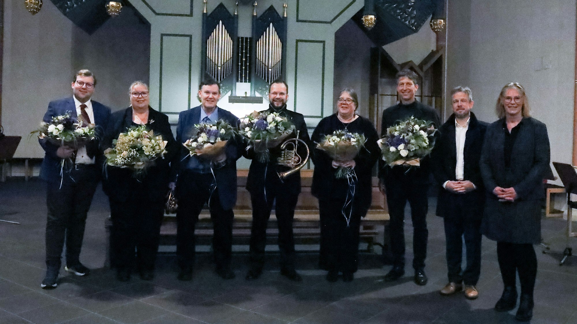 Acht Menschen schauen in Richtung der Kamera, sechs von ihnen halten Blumensträuße.