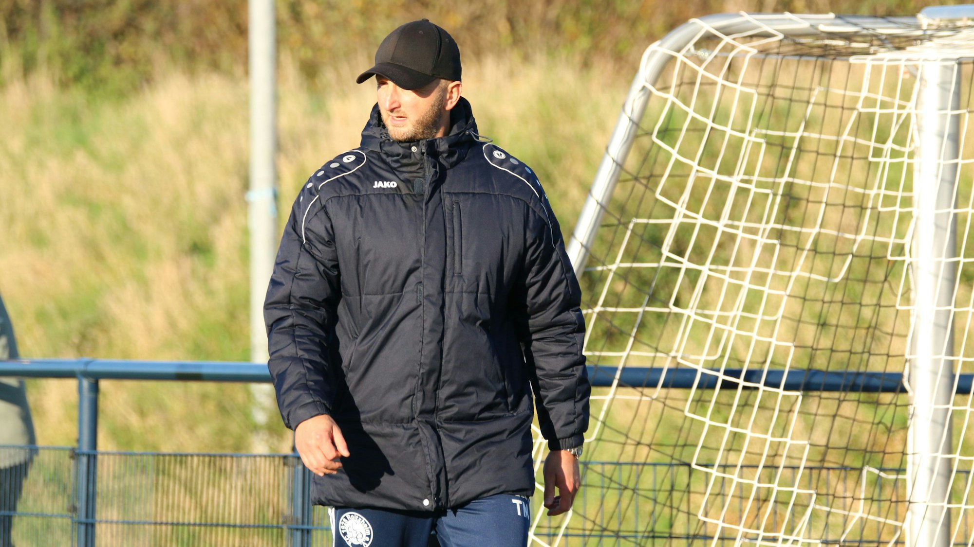 Das Bild zeigt den Coach des SC Roitzheim an der Seitenlinie. Er trägt eine schwarze Kappe und eine schwarze Winterjacke.
