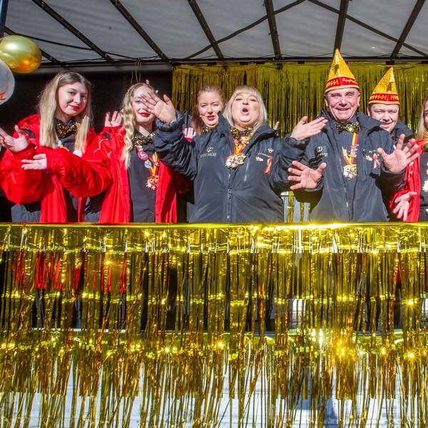 Menschen mit Narrenkappen feiern auf einer Bühne.