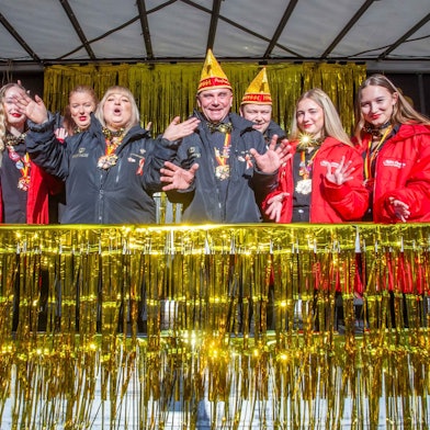 Menschen mit Narrenkappen feiern auf einer Bühne.