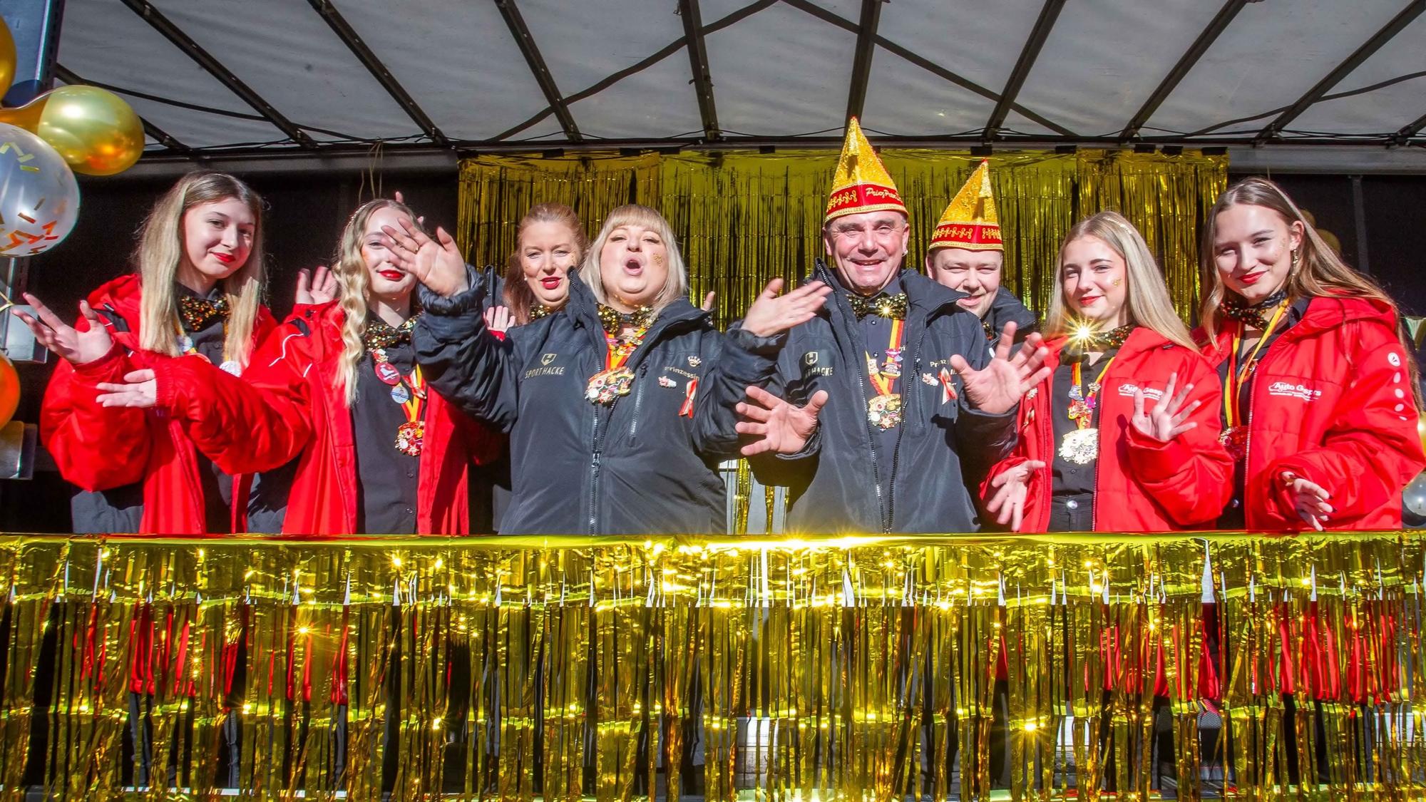 Menschen mit Narrenkappen feiern auf einer Bühne.