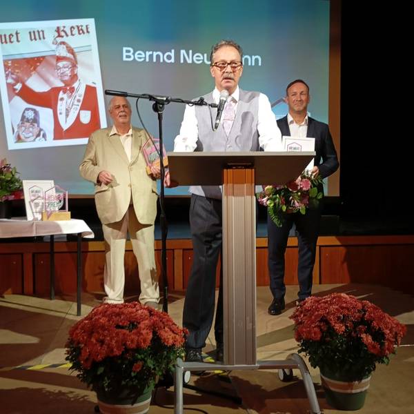 Bernd Neumann trägt eine graue Weste und ein weißes Hemd. Er steht an einem Pult und spricht in ein Mikrofon.