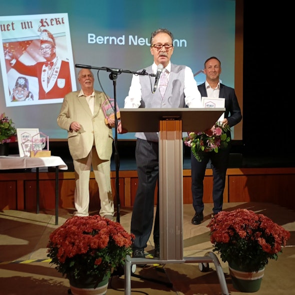 Bernd Neumann trägt eine graue Weste und ein weißes Hemd. Er steht an einem Pult und spricht in ein Mikrofon.