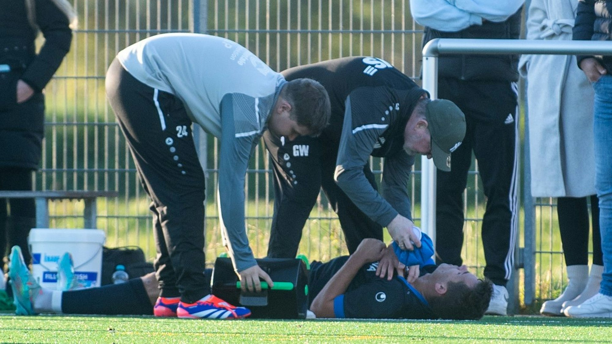 Das Bild zeigt Helge Hohl auf dem Boden liegend. Vernichs Trainer hilft mit einem Kühlakku aus.