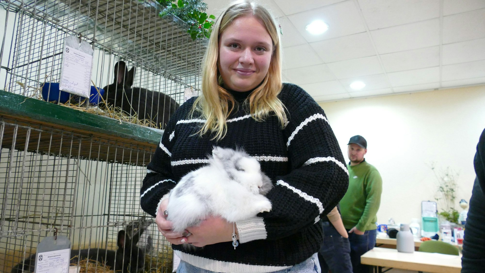 Eine junge Frau hält ein weiß-graues, flauschiges Kaninchen im Arm.