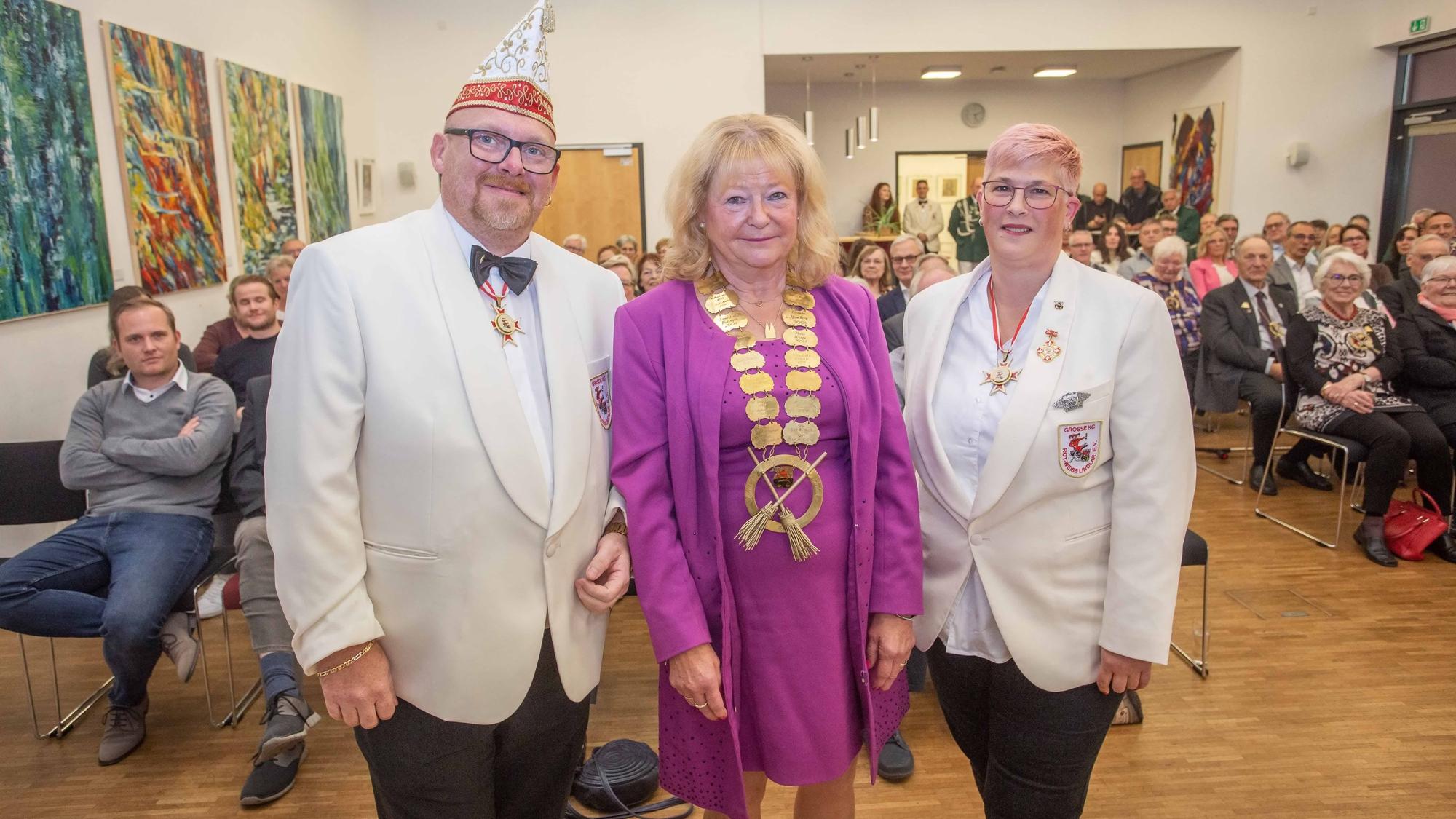 Eine Frau steht, mit einem goldenen Orden um den Hals, mit zwei Männern eines Karnevalsvereins beisammen.