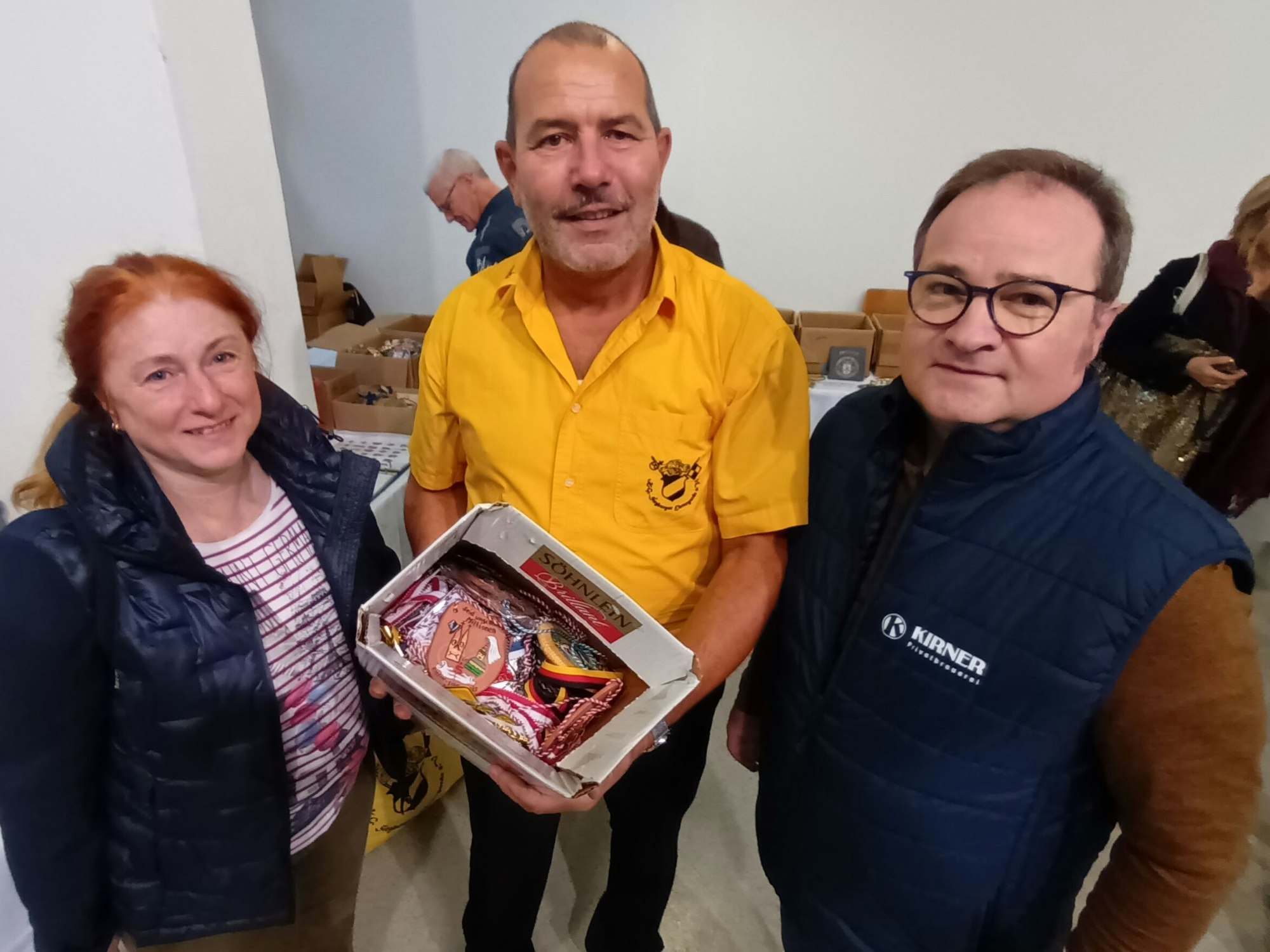 Zwei Männer und eine Frau mit einer Kiste voller Karnevalsorden