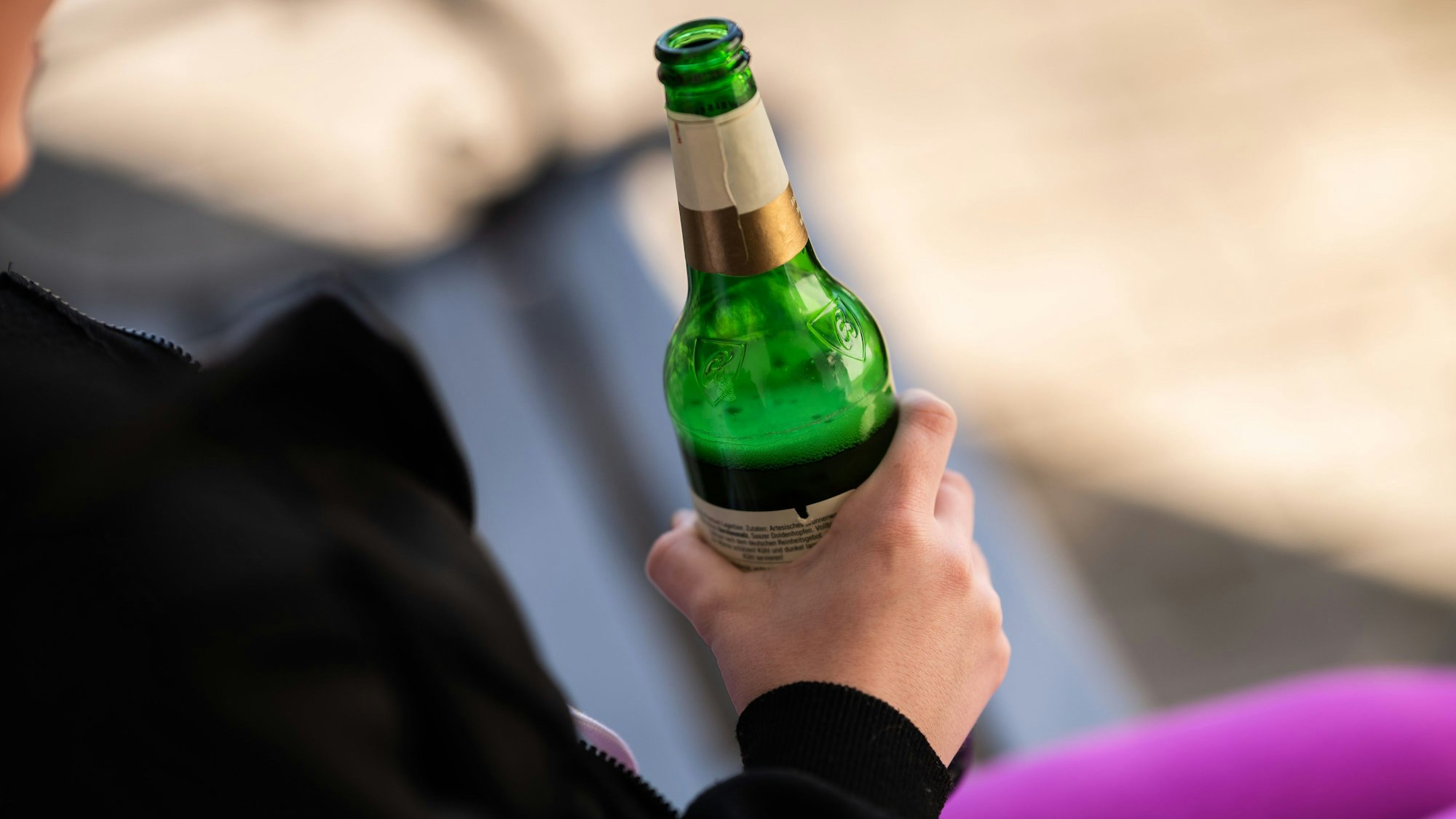 Eine Jugendliche hält vor ihrem Haus eine Flasche Bier in der Hand.