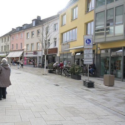 Rechts und links der Straße stehen die Verkehrsschilder Fußgängerzone. Eine Frau daneben.
