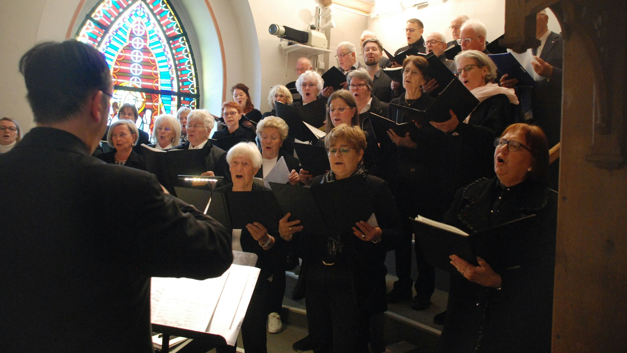 Ein Chor singt, mit aufgeschlagenen Gesangsbüchern in den Händen, in einer Kirche.