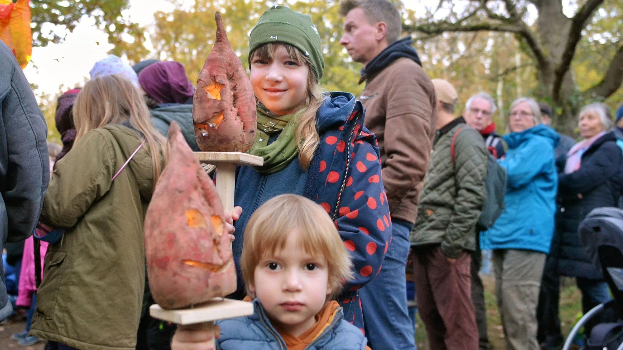 Zwei Kinder halten Rübenlaternen in die Luft.