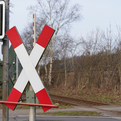 Blick auf einen Bahnübergang mit Andreaskreuzen, Ampeln und den Bahngleisen.