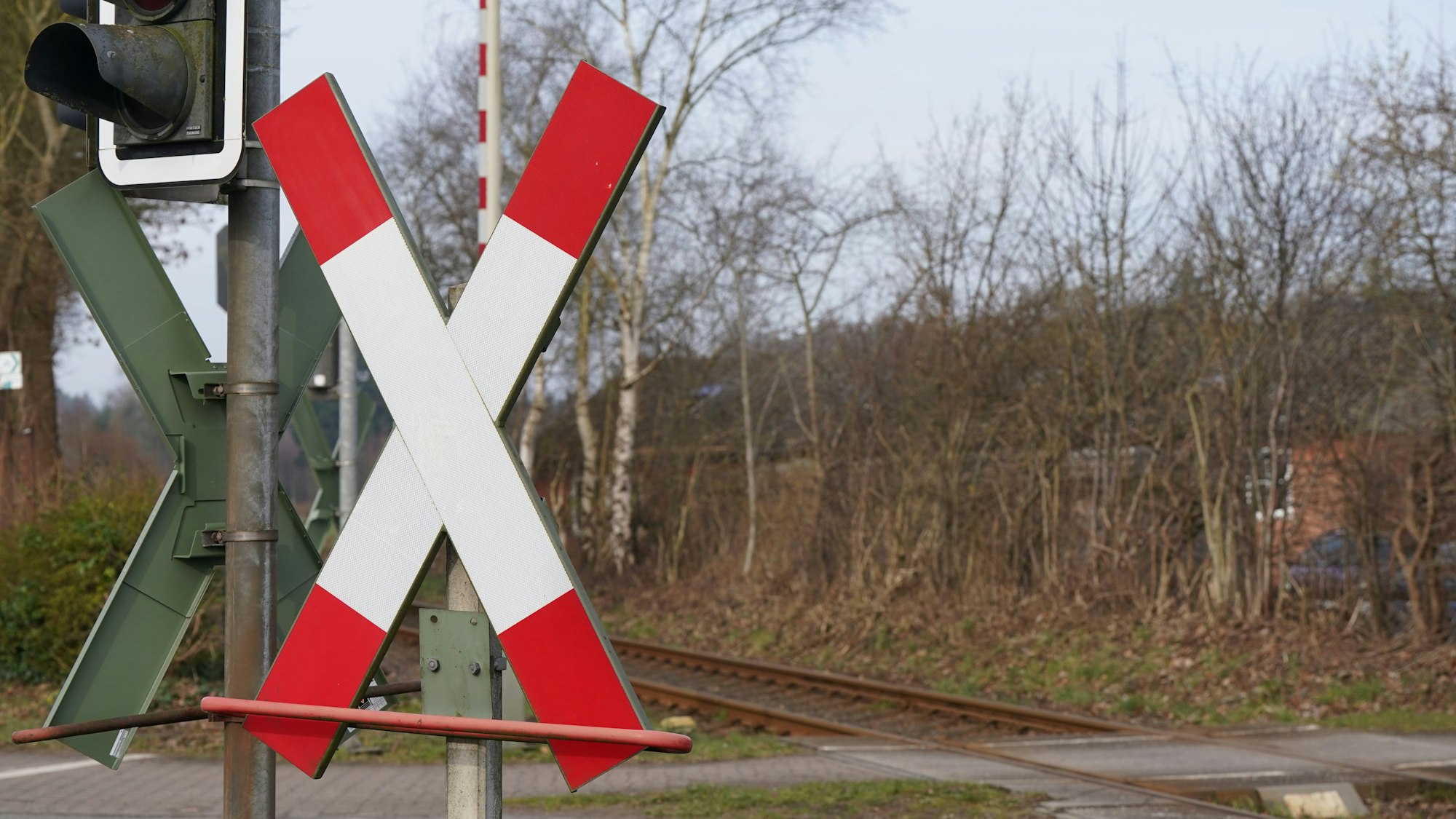 Blick auf einen Bahnübergang mit Andreaskreuzen, Ampeln und den Bahngleisen.