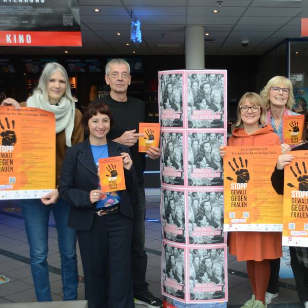 Eine Gruppe von sechs Frauen und zwei Männern hat sich zum Gruppenfoto aufgestellt. Sie tragen orange Plakate mit einer schwarzen zum Stopp gespreizten Handfläche.