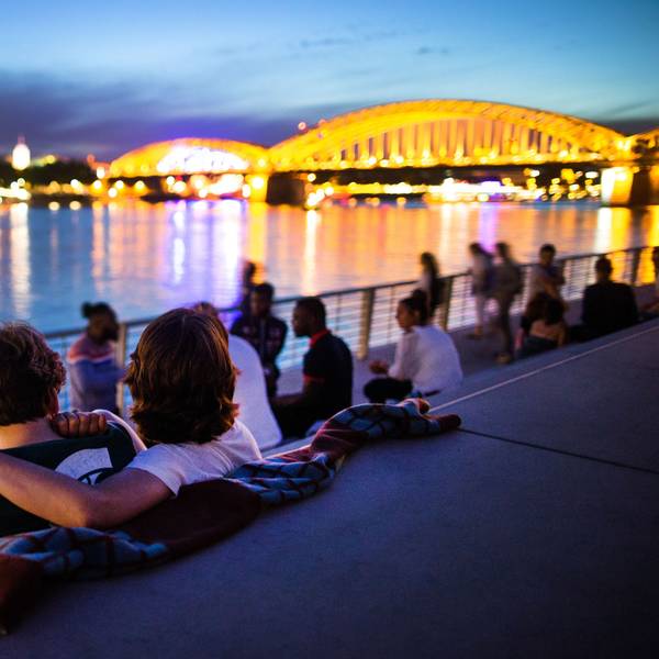 Menschen sitzen bei Sonnenuntergang auf dem neuen Rheinboulevard am Rhein in Köln (Nordrhein-Westfalen) mit Blick auf den Dom.