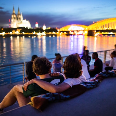 Menschen sitzen bei Sonnenuntergang auf dem neuen Rheinboulevard am Rhein in Köln (Nordrhein-Westfalen) mit Blick auf den Dom.