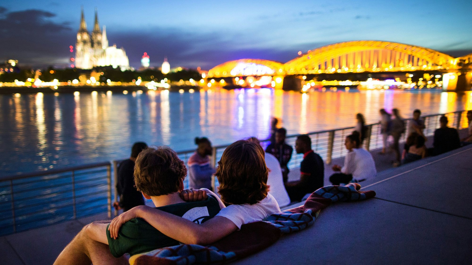 Menschen sitzen bei Sonnenuntergang auf dem neuen Rheinboulevard am Rhein in Köln (Nordrhein-Westfalen) mit Blick auf den Dom.