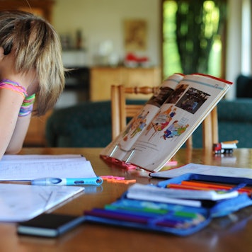 Ein Junge hält sich beim Erledigen seiner Hausaufgaben den Kopf. Vor und neben ihm liegen Schulhefte.