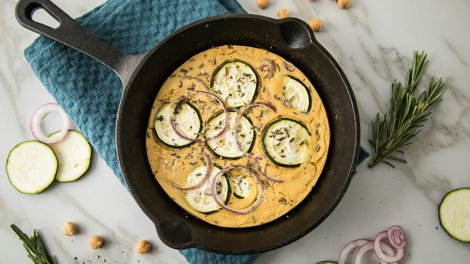 Socca ist eine südfranzösische Fladenbrot-Spezialität. Hier ist die Socca-Pizza aus Kichererbsenmehl mit Zucchini, Rosmarin und roten Zwiebeln belegt.
