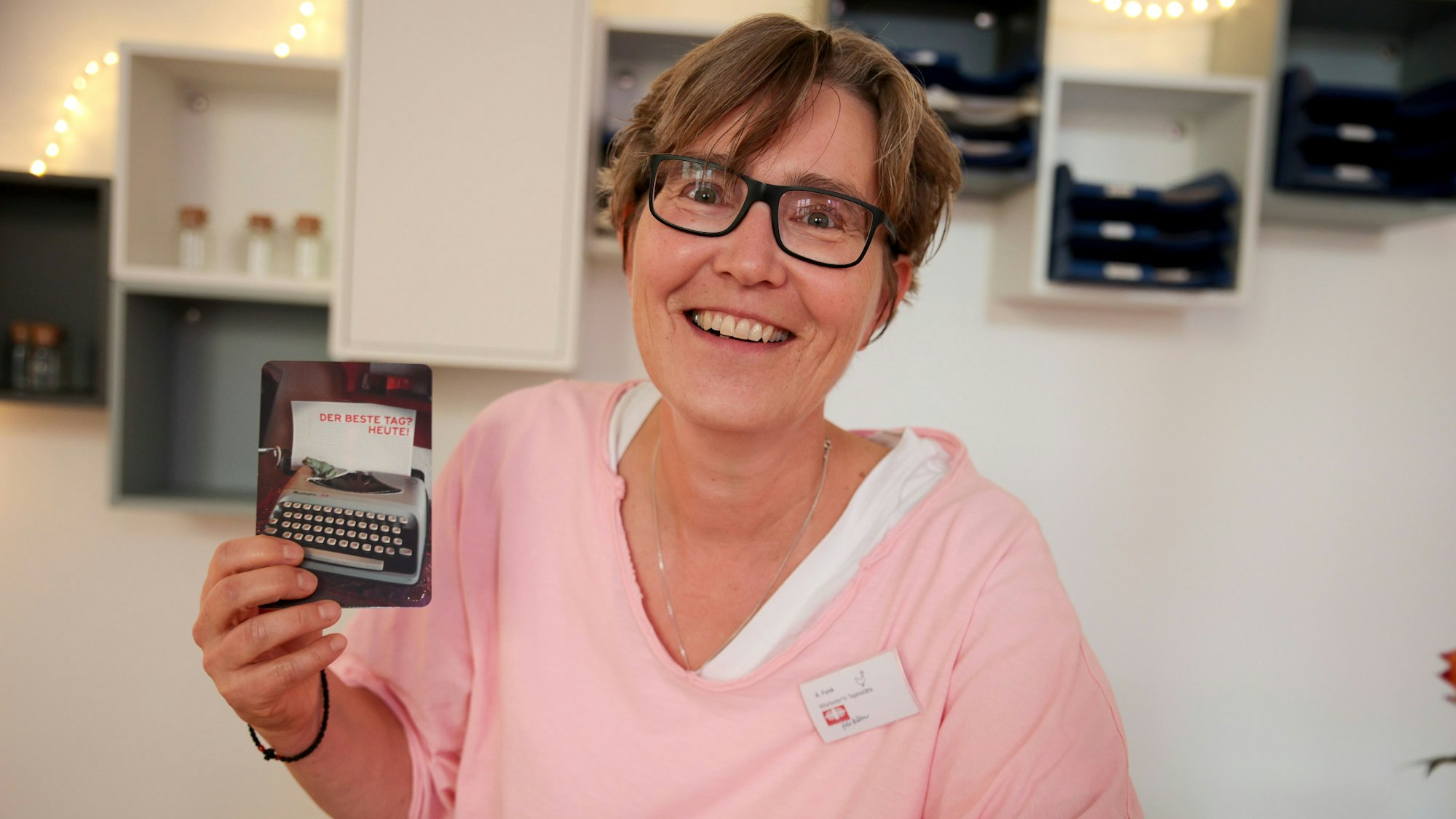 Andrea Funk trägt einen rosa Pullover und hält eine Karte in der rechten Hand.