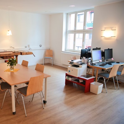 Ein Raum mit Werkbank, vier PCs und einem Tisch mit sechs Stühlen.