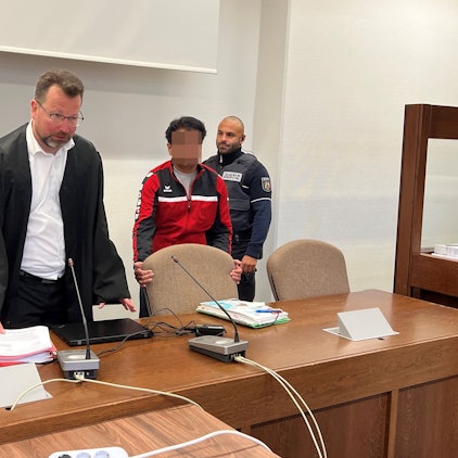 Der Angeklagte mit Verteidiger Philipp Thiée und einem Wachtmeister beim Prozessauftakt im Landgericht Köln