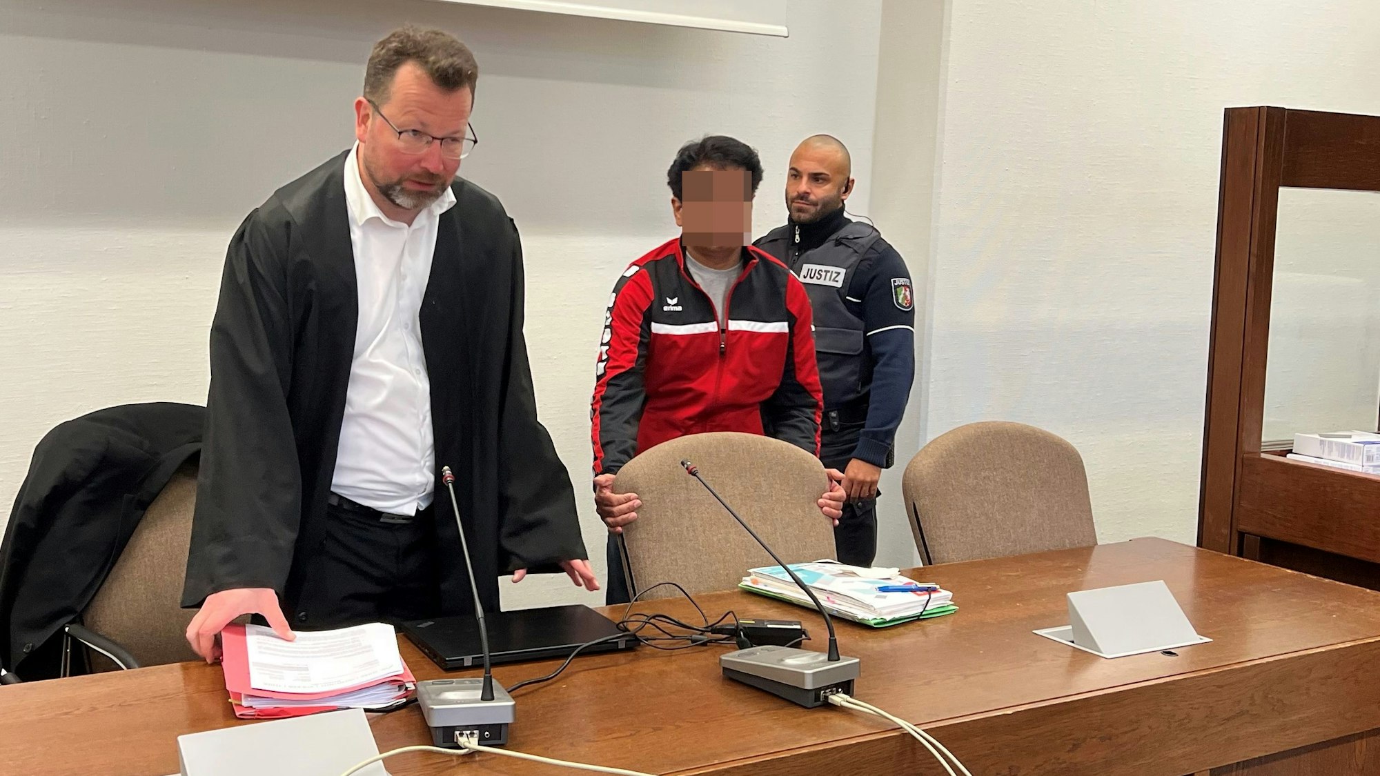 Der Angeklagte mit Verteidiger Philipp Thiée und einem Wachtmeister beim Prozessauftakt im Landgericht Köln