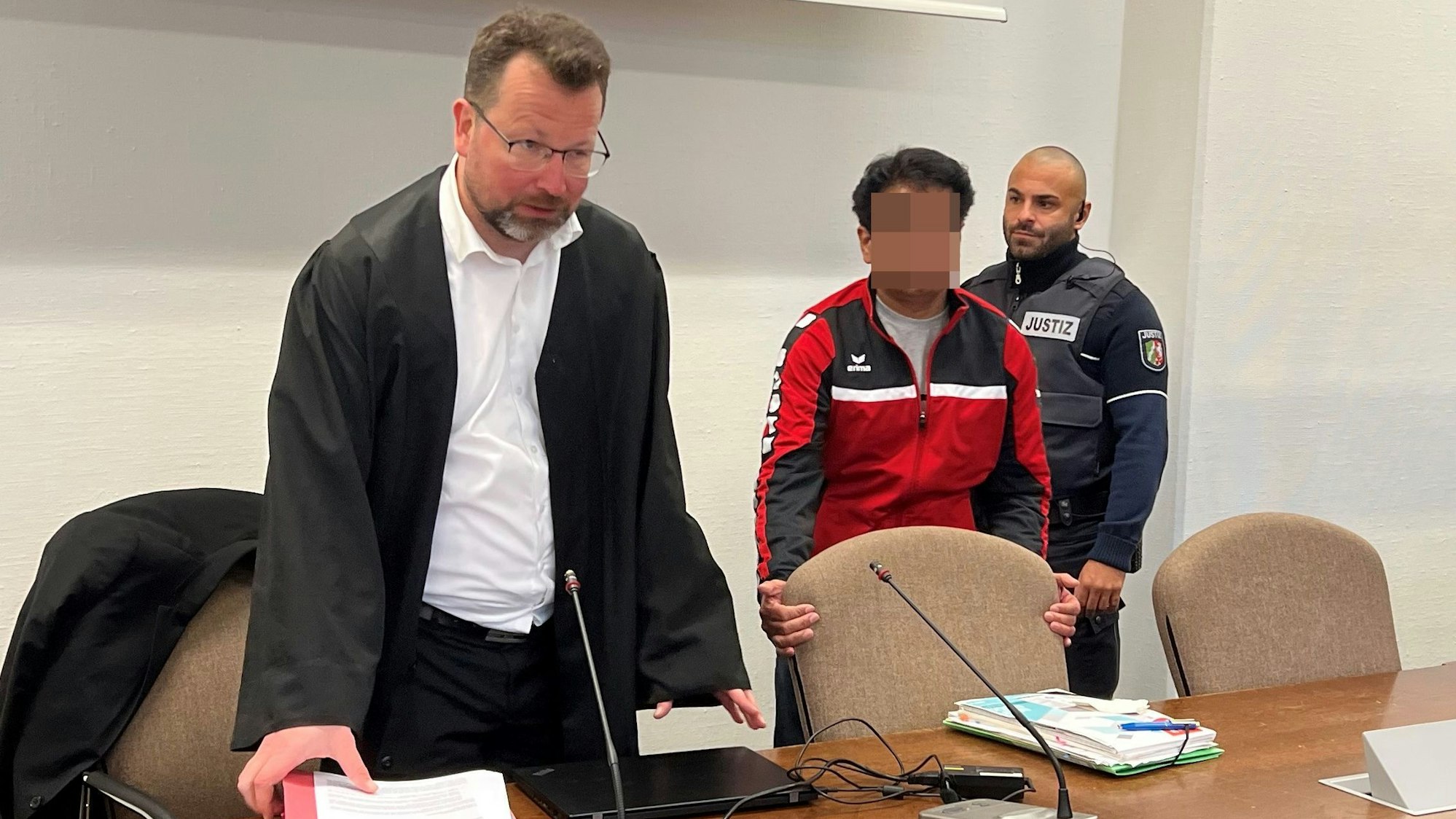 Der Angeklagte mit Verteidiger Philipp Thiée und einem Wachtmeister beim Prozessauftakt im Landgericht Köln