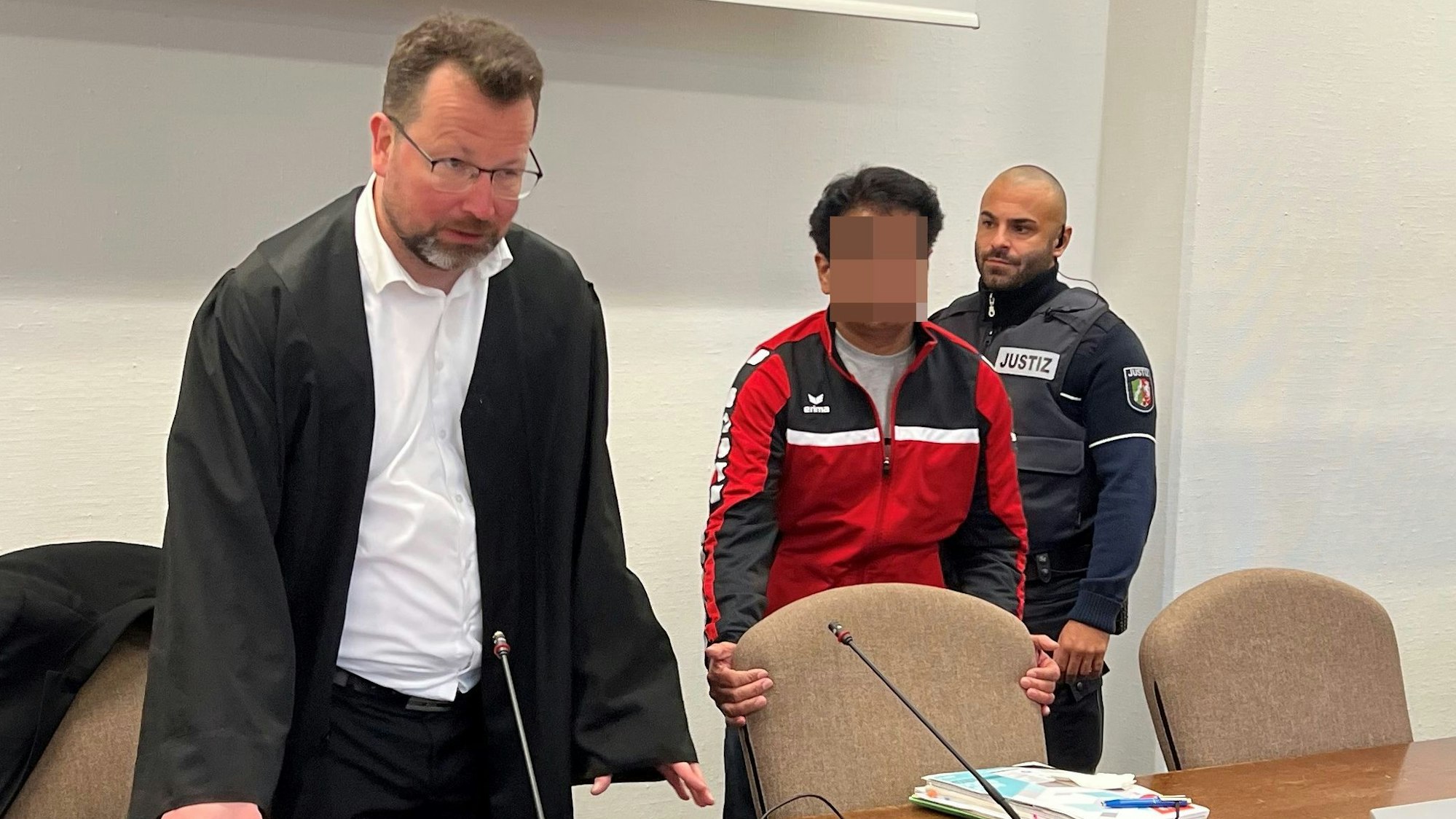 Der Angeklagte mit Verteidiger Philipp Thiée und einem Wachtmeister beim Prozessauftakt im Landgericht Köln
