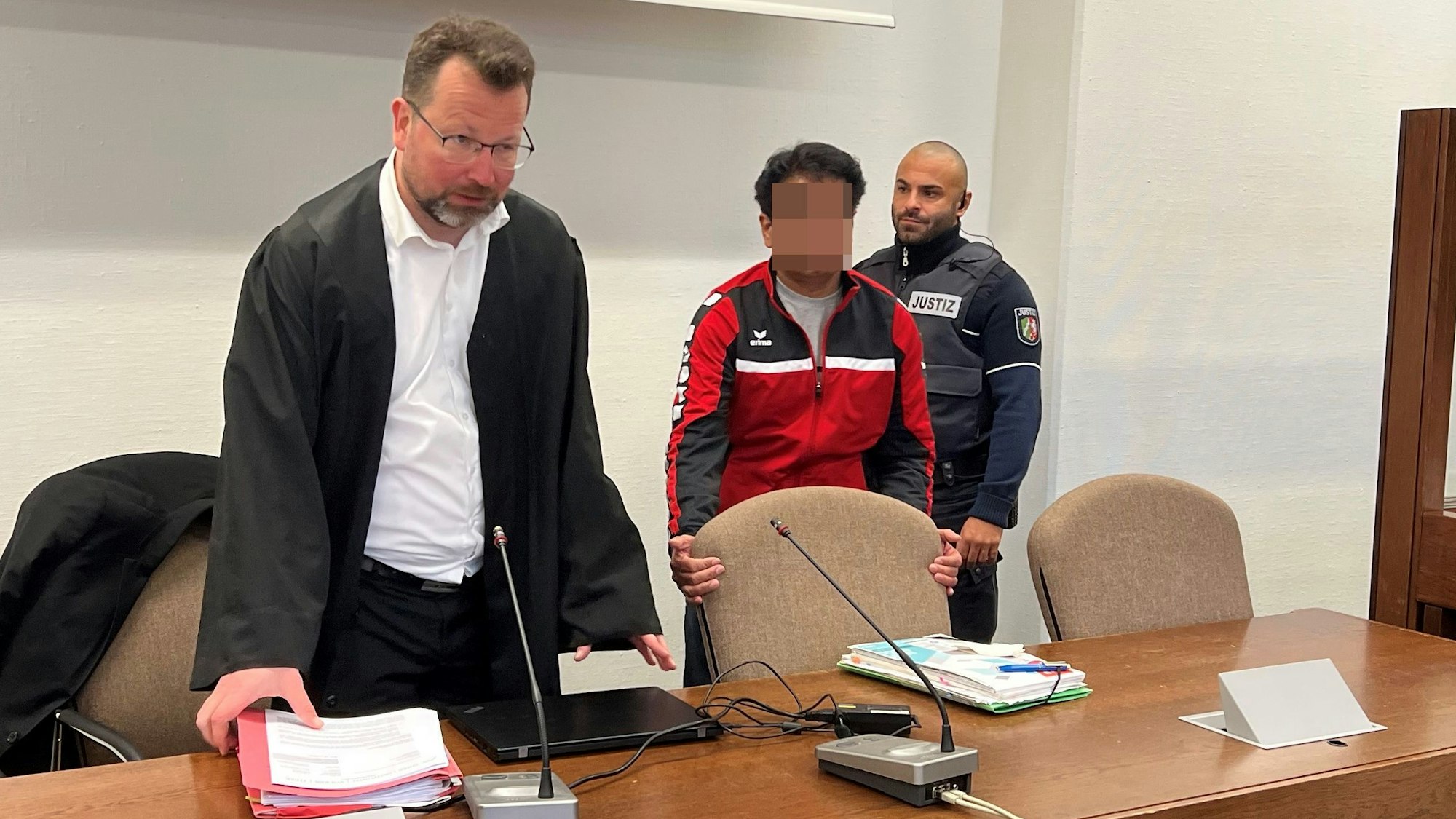 Der Angeklagte mit Verteidiger Philipp Thiée und einem Wachtmeister beim Prozessauftakt im Landgericht Köln