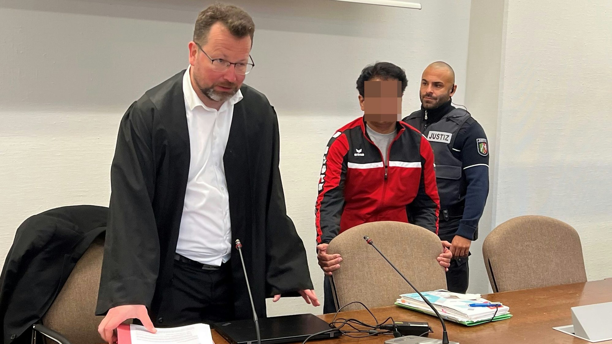 Der Angeklagte mit Verteidiger Philipp Thiée und einem Wachtmeister beim Prozessauftakt im Landgericht Köln.