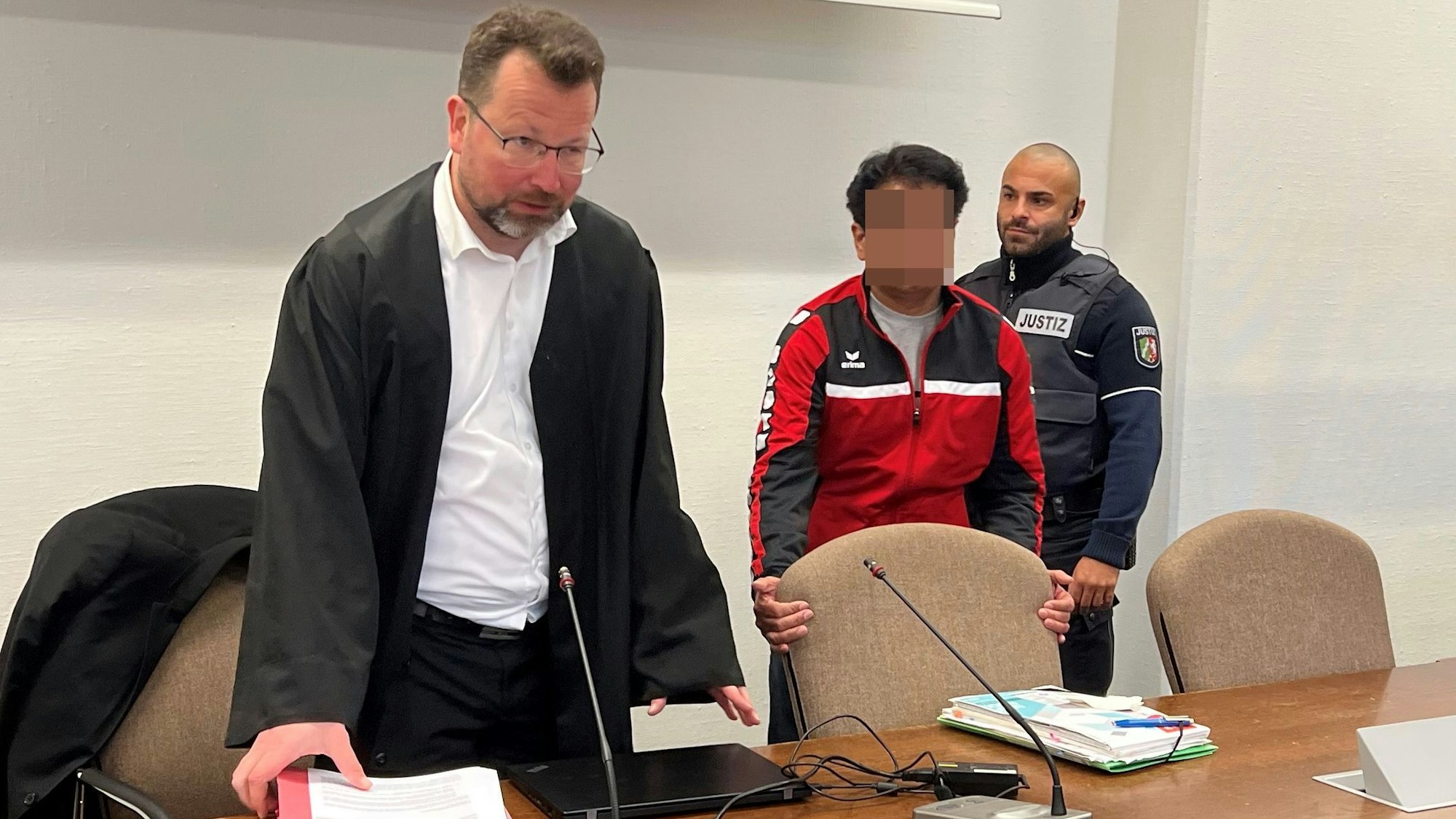 Der Angeklagte mit Verteidiger Philipp Thiée und einem Wachtmeister beim Prozessauftakt im Landgericht Köln