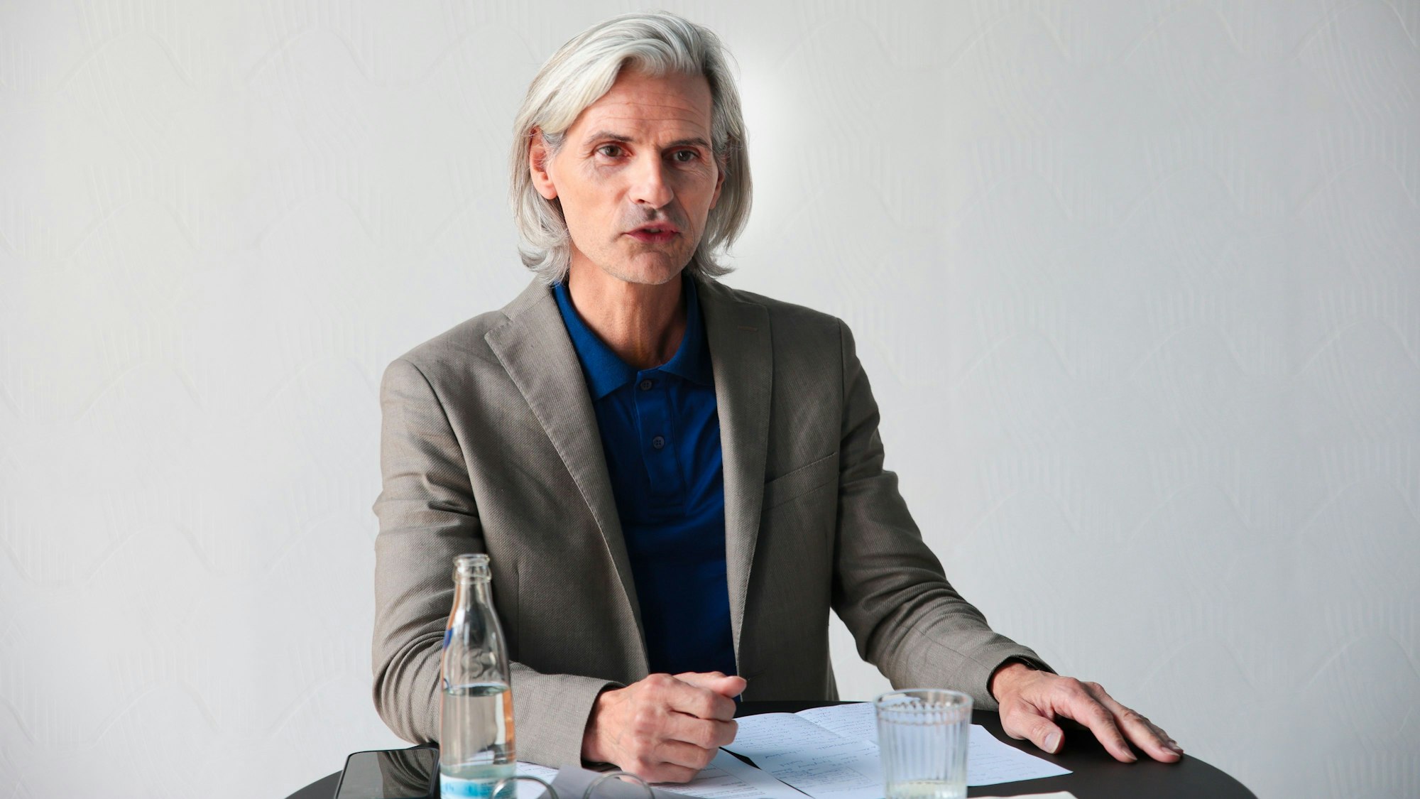 Stefan Charles steht an einem Pult. Er trägt ein graues Sakko zum dunkelblauen Hemd.