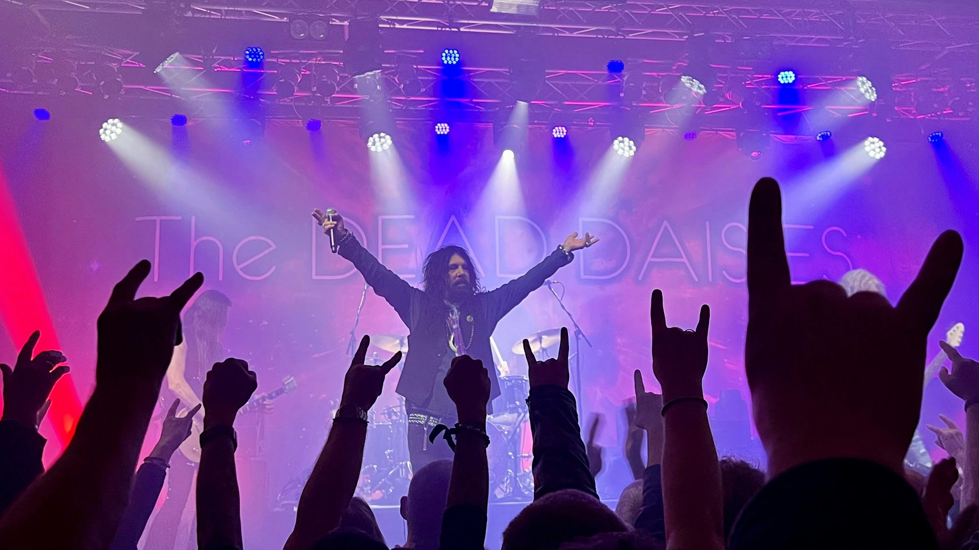 Zuschauer im Publikum zeigen die Pommesgabel, im Hintergrund steht Sänger John Corabi.