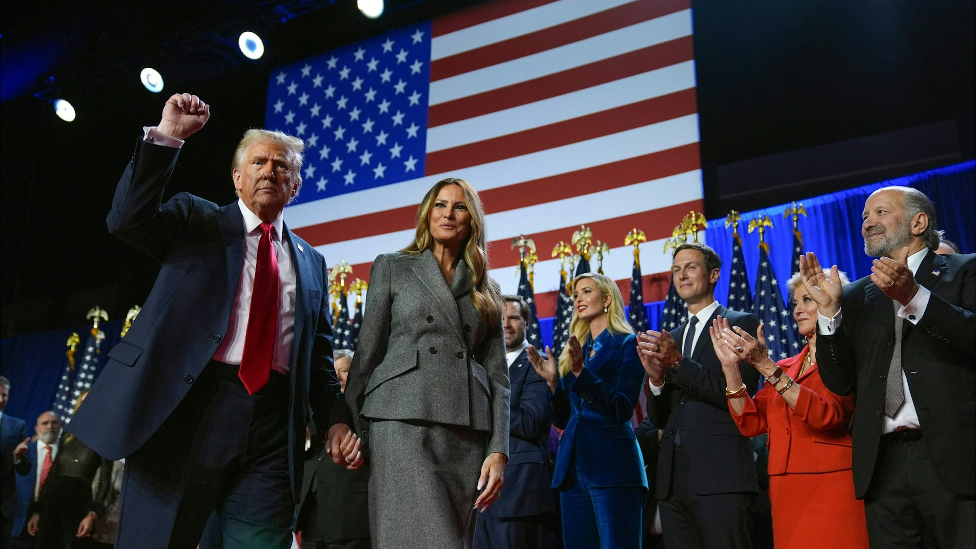 Donald Trump gestikuliert, während er mit der ehemaligen First Lady Melania Trump bei einer Wahlparty im Palm Beach Convention Center über die Bühne geht