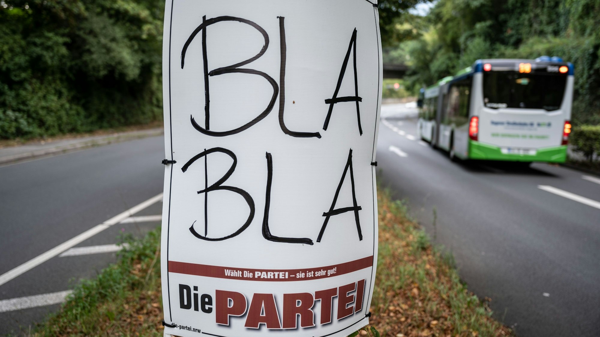 Ein Plakat zur Kommunalwahl in Nordrhein-Westfalen von ·Die Partei· mit der Aufschrift ·Bla Bla· ist auf dem Mittelstreifen einer Strasse an einem Baum befestigt.