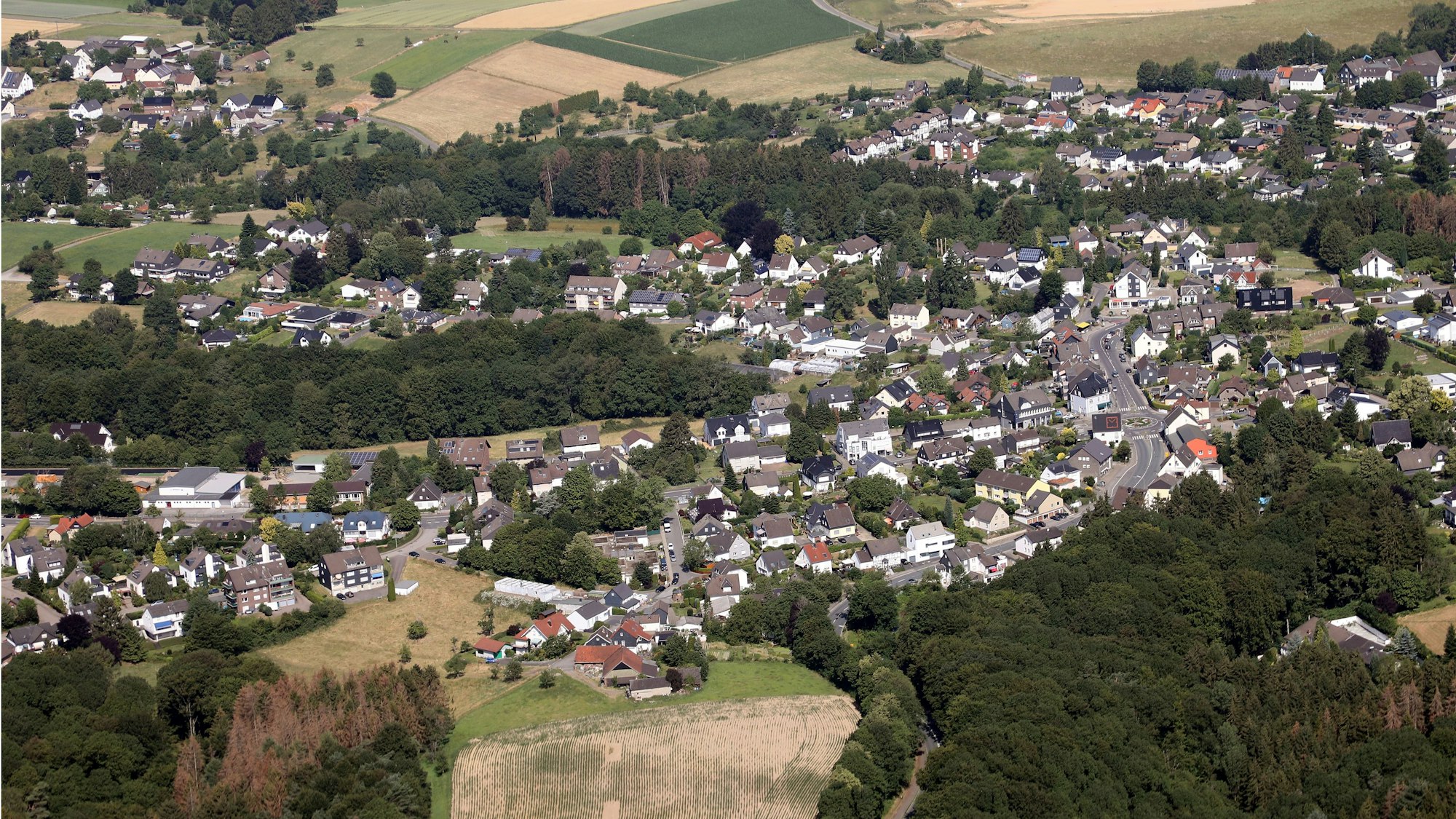 Ein Luftbild von Odenthal-Blecher. Man sieht den zentralen Kreisverkehr, links davon die Bergstraße und im unteren Bildteil die Serperntinen nach Altenberg.
