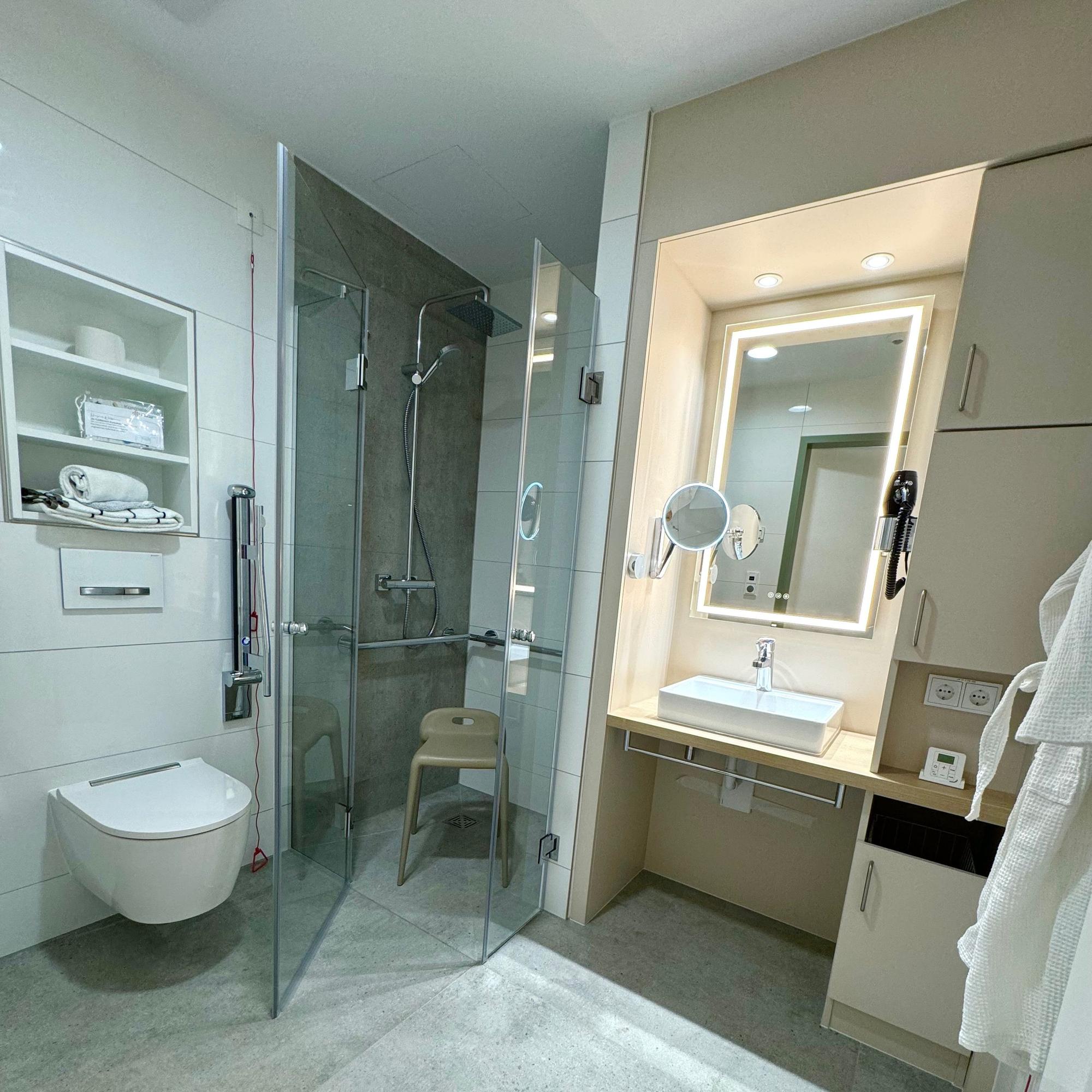 Zu sehen ist ein Badezimmer mit Dusche. In der Dusche steht ein Hocker.